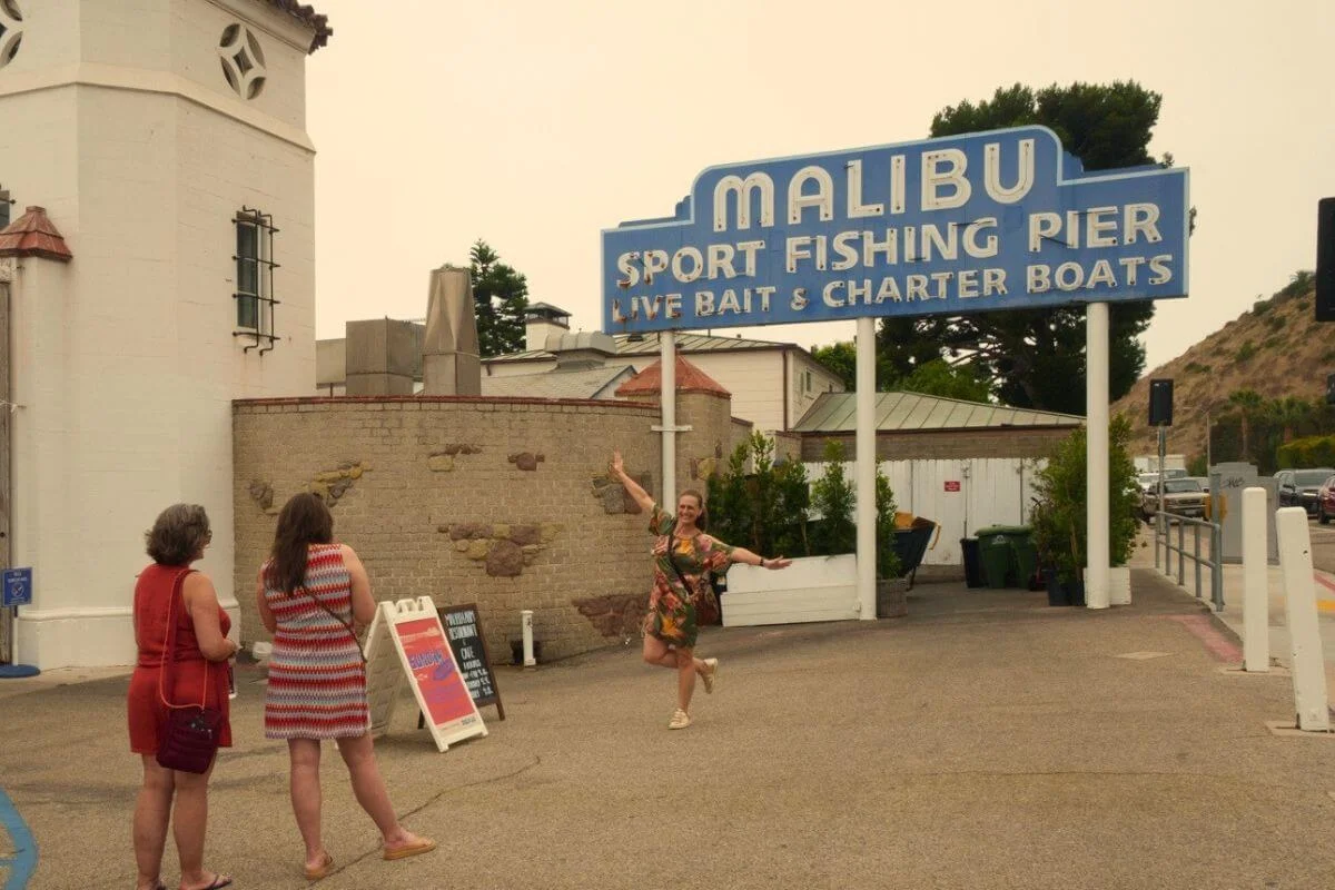 Tourists posing by Malibu Sport Fishing Pier sign