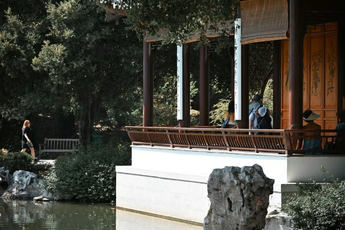 Traditional Chinese pavilion beside a calm pond with visitors and lush garden trees in Pasadena