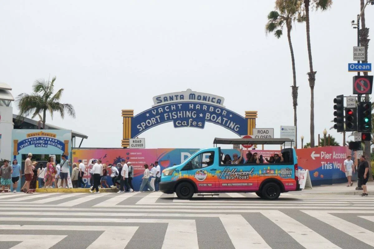 Hollywood Bus Tours colorful van passing in front of the iconic Santa Monica Yacht Harbor arch sign