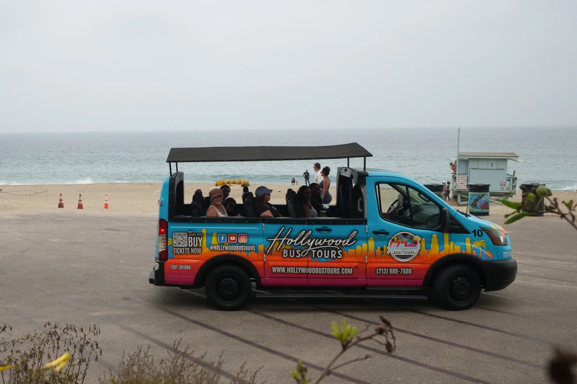Hollywood Bus Tours open-air sightseeing bus parked along Malibu Beach during a scenic Los Angeles tour.