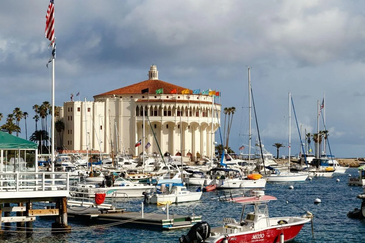 Catalina Casino surrounded by boats in the harbor with colorful flags and cloudy skies