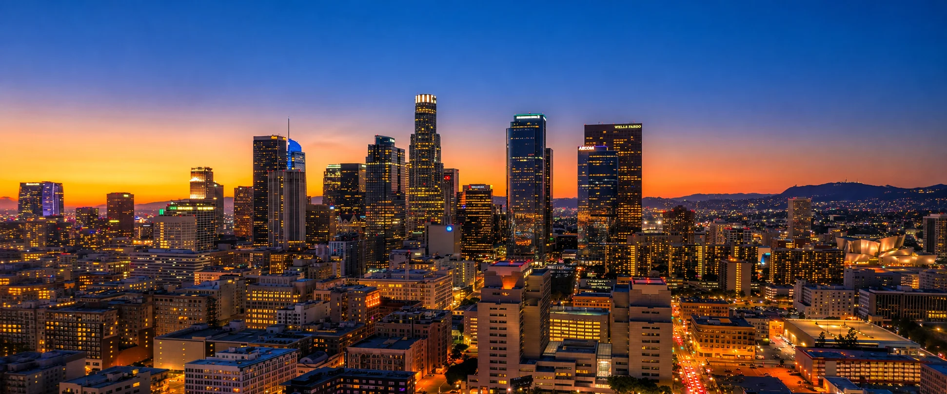 Downtown Los Angeles skyline lit up at twilight with an orange and blue sunset behind the city buildings