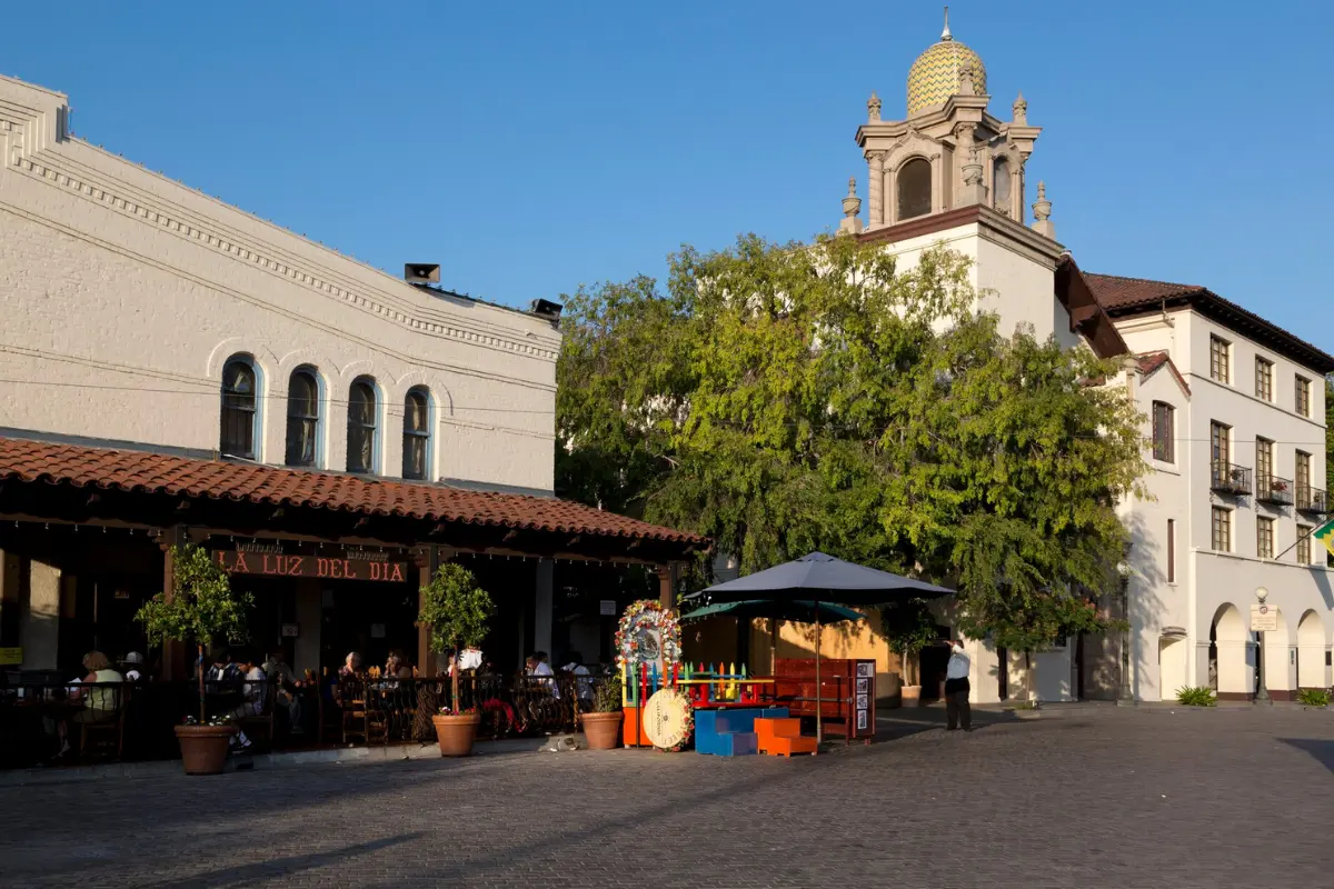 La Luz del Dia restaurant with a red tile roof and outdoor diners beside a historic white tower with a tiled dome at El Pueblo plaza